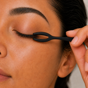 Close-up of a black lash tool pressing along fused lashes on a closed eye