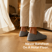 A pair of slipper socks on the floor of a hotel room beside a bed