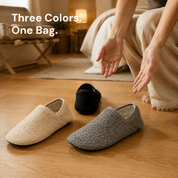 Three pairs of slipper socks in cream, grey and black laid out on a bed