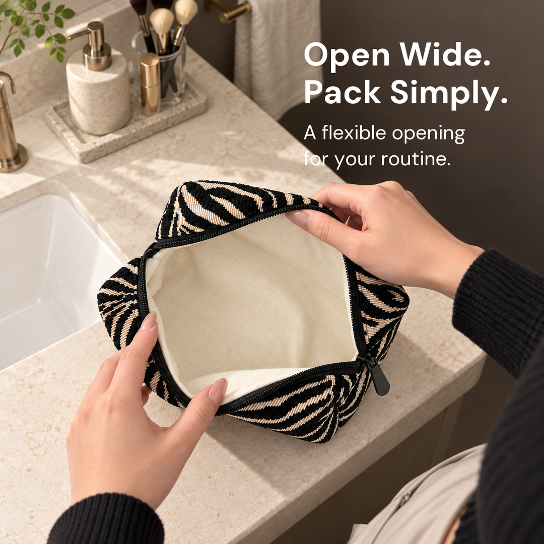 Hands spread open the black and cream zebra pouch beside a bathroom sink, revealing its cream interior.