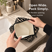 Hands spread open the black and cream zebra pouch beside a bathroom sink, revealing its cream interior.