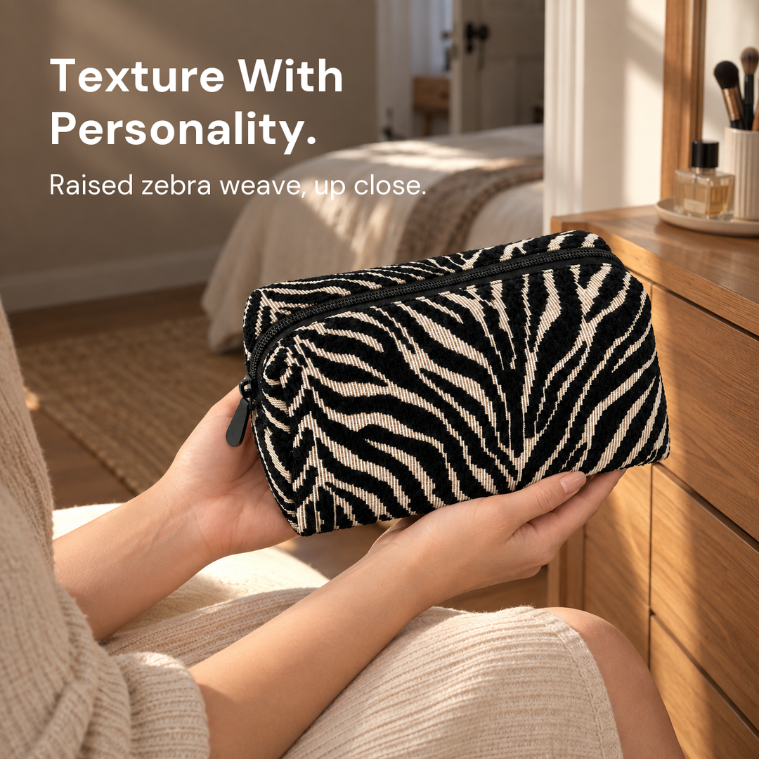 Hands hold a black and cream zebra pouch beside a wooden dresser, showing its raised weave.