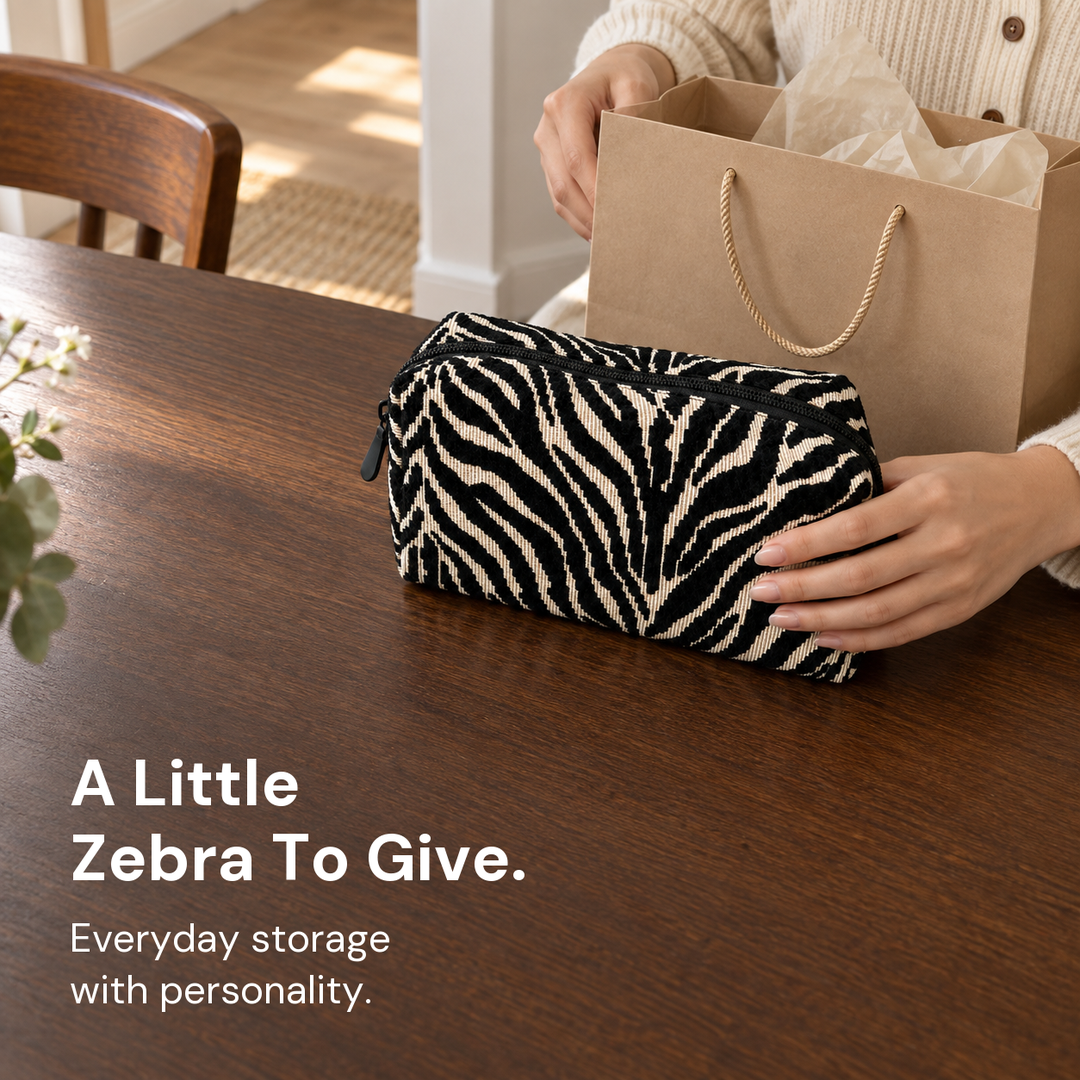A black and cream zebra pouch beside a kraft gift bag and tissue paper on a wooden table.