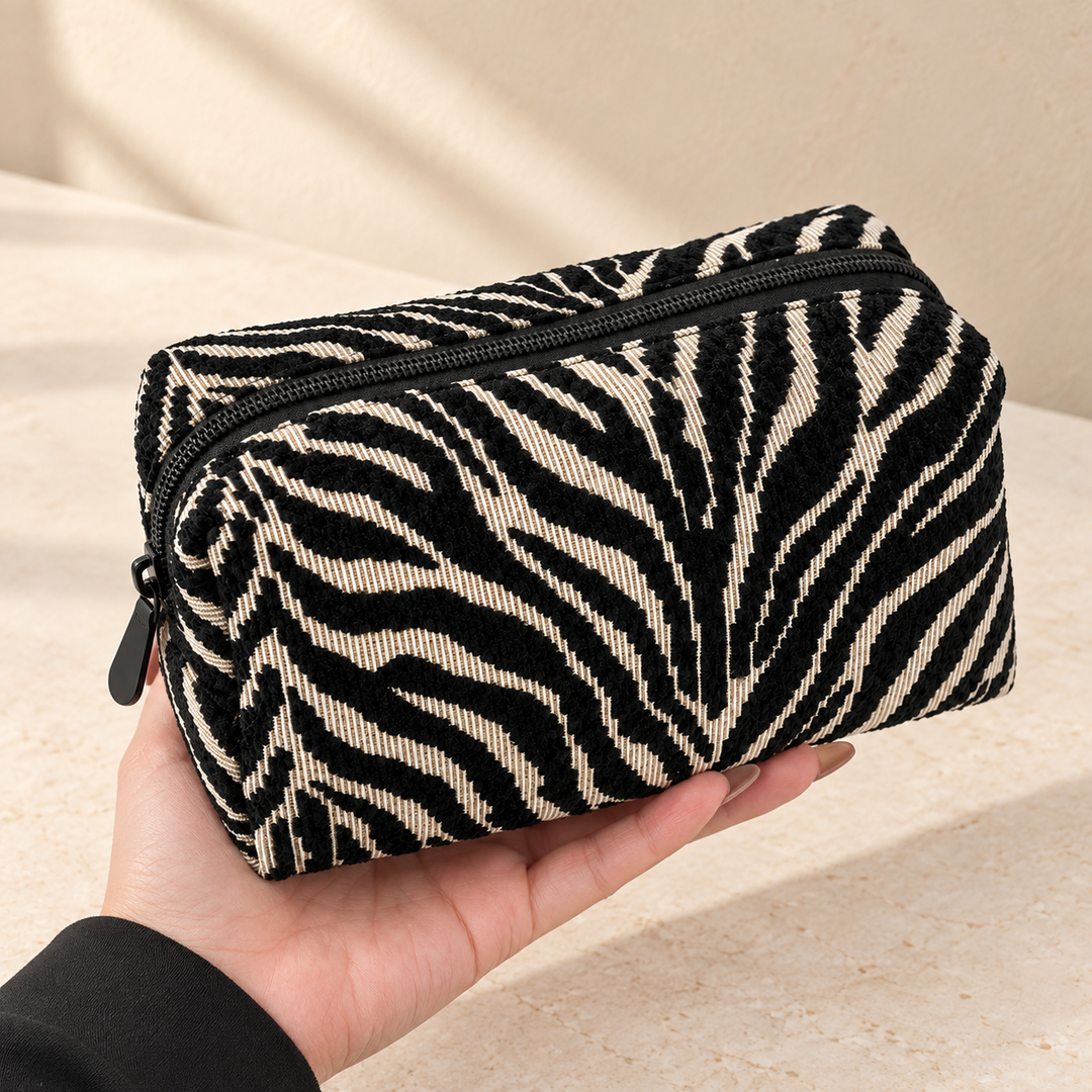 A hand supports a closed black and cream zebra pouch, with its dark top zipper visible.