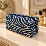 Blue zebra makeup pouch with cream stripes and a dark zipper on a sunlit vanity.