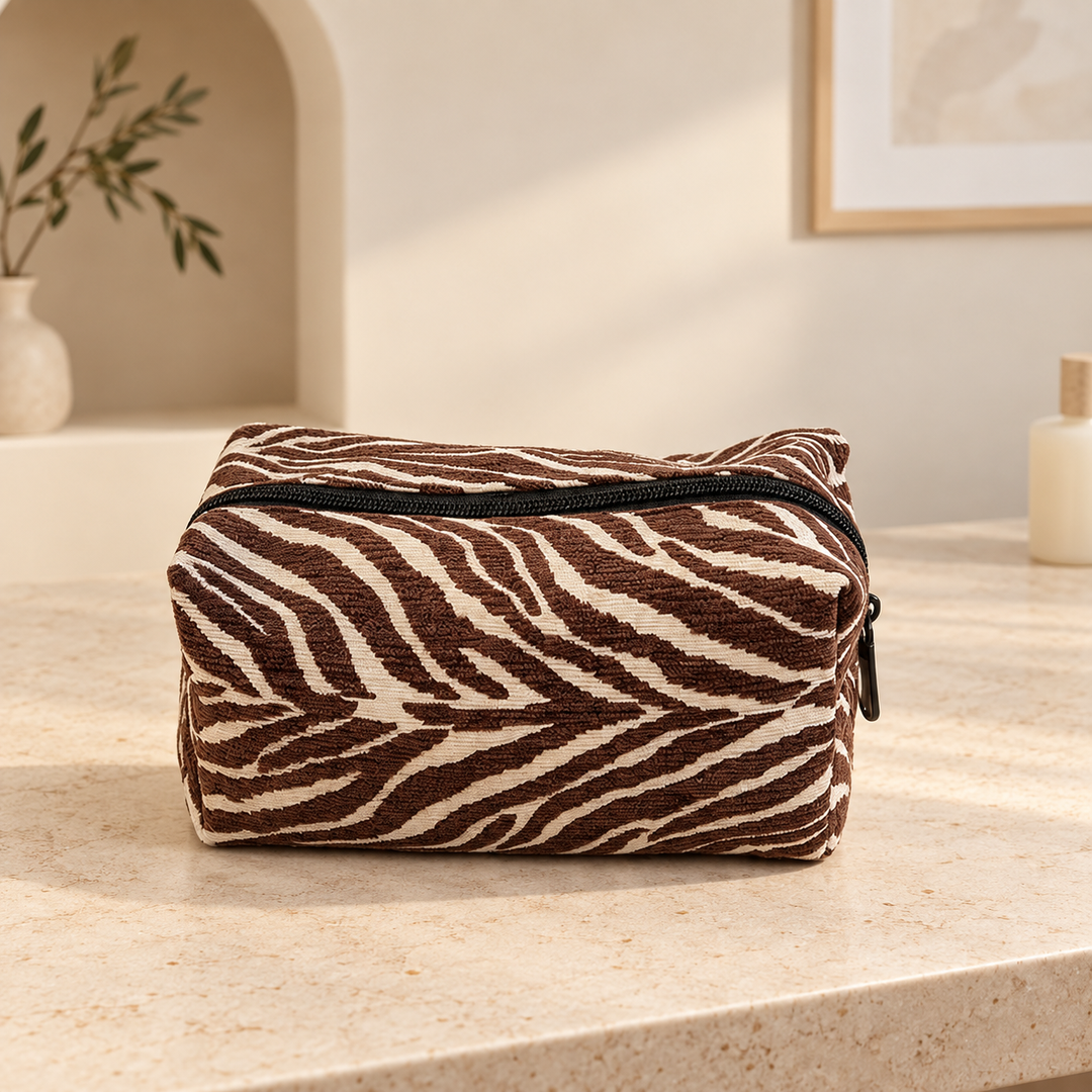 Brown zebra makeup pouch with cream stripes standing closed on a pale stone vanity.