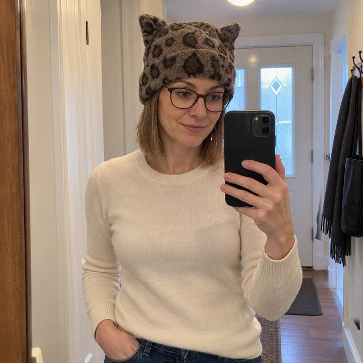 Illustrative hall-mirror selfie wearing a Leopard Cleo cat ear hat and a cream sweater.