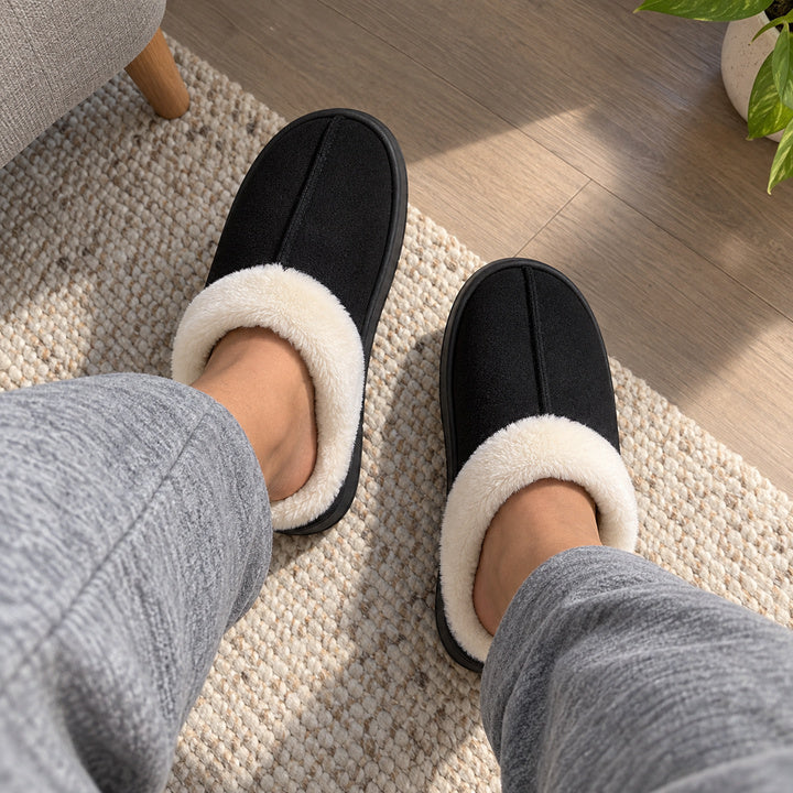 Black Haven slippers worn with grey trousers, photographed looking down at both feet.