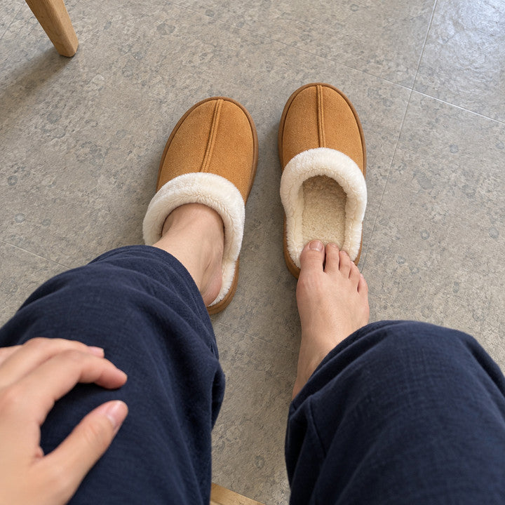 Looking down from a seated wearer: one Chestnut Haven slipper on, with the other waiting at their bare toes.