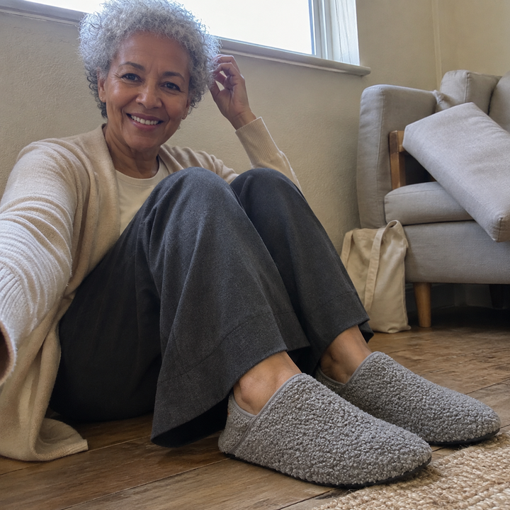 A woman sitting on the floor by a window, knees up, wearing barefoot travel slipper socks