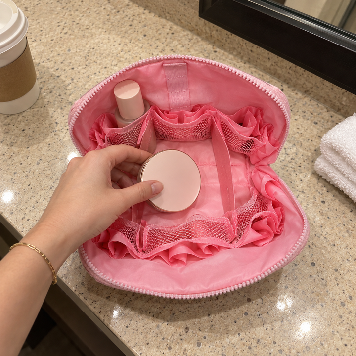 A hand places a compact inside open Pink Clara on a hotel vanity