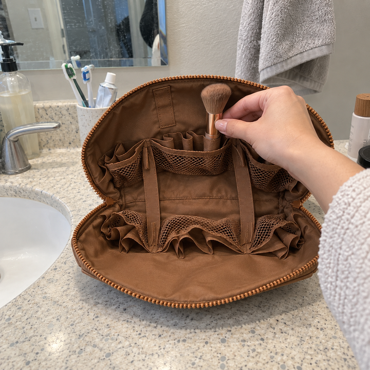A hand inserts a makeup brush into a fabric loop inside open Brown Clara beside a bathroom sink