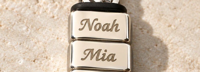 Close-up of two silver name blocks on the woven chain, engraved Noah and Mia, one name on each