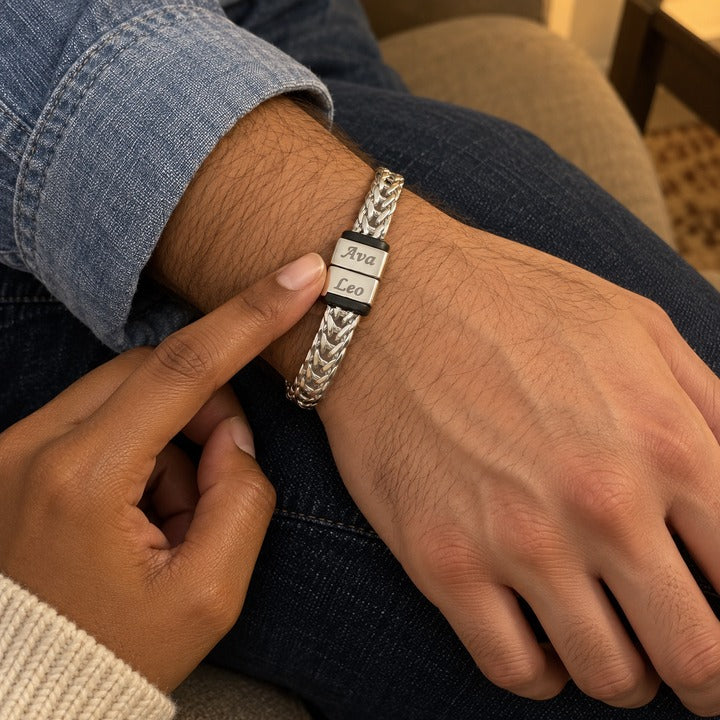 A woman's fingertip resting on the silver Harbor name bracelet with two names on a man's wrist, on the sofa, everyday phone photo
