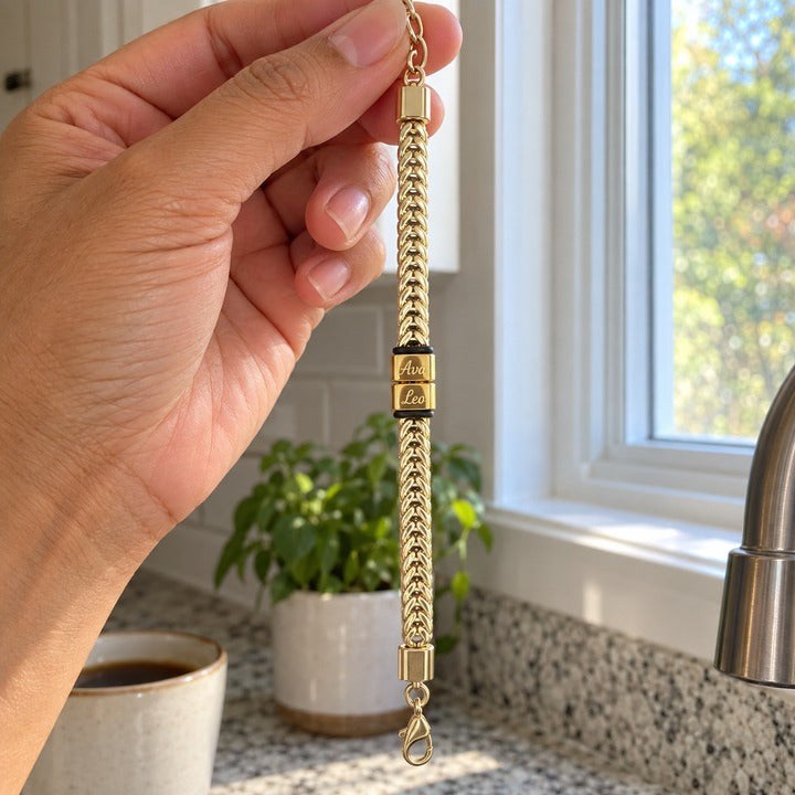 The gold Harbor name bracelet held up by its extender chain between a woman's fingers by a kitchen window, everyday phone photo