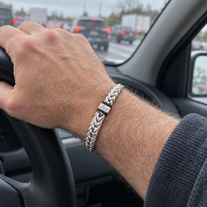 A man driving with the silver Harbor name bracelet on the wrist of his hand on the steering wheel, everyday phone photo