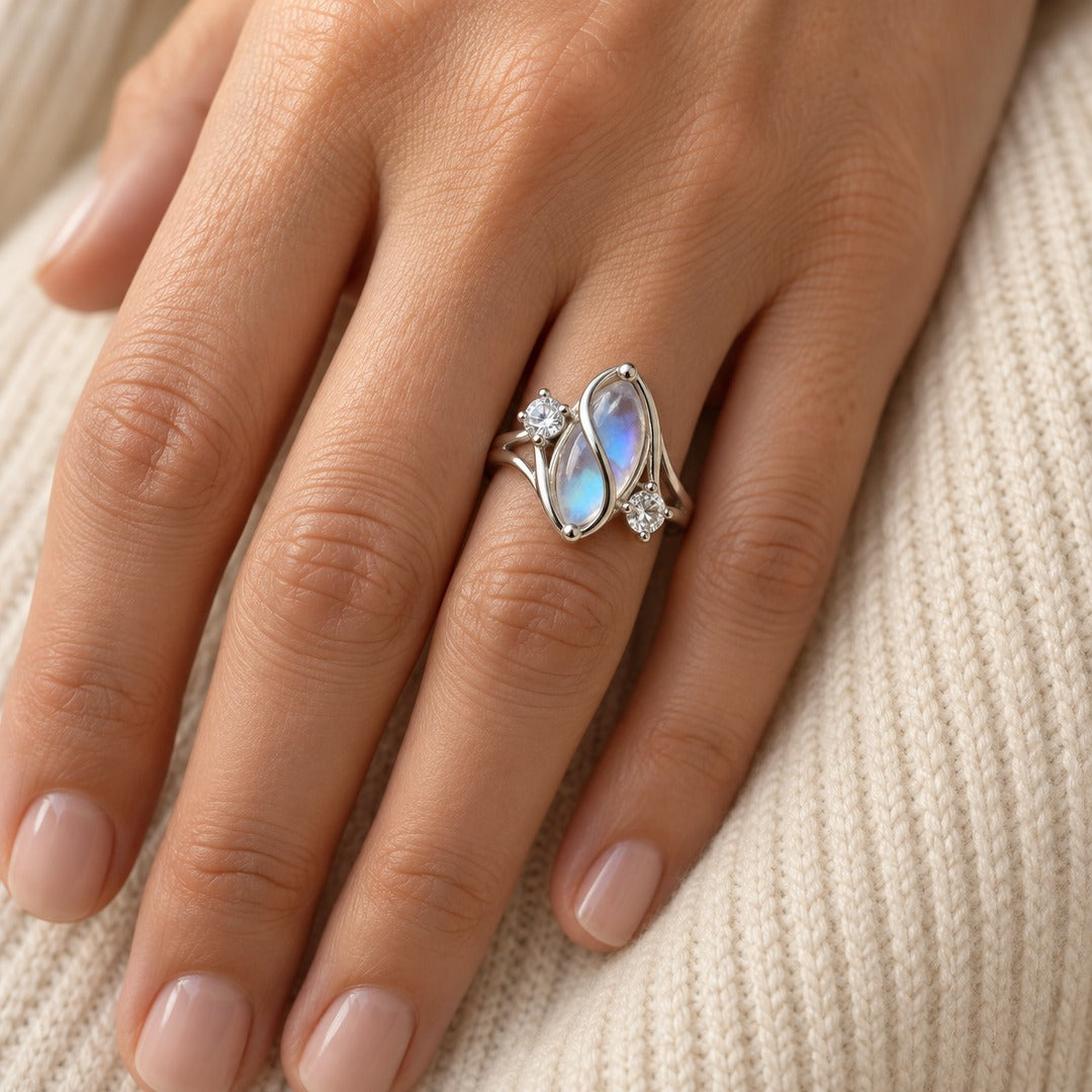 Close-up of the simulated moonstone ring on a hand resting on a cream knit, the soft blue sheen in the stone