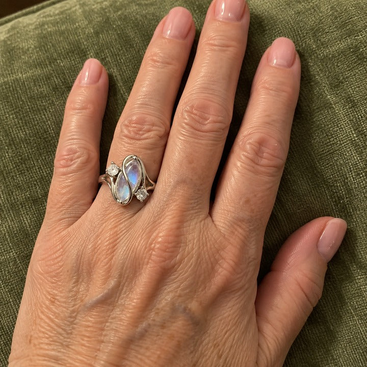 Hand resting on a green velvet couch cushion, wearing the simulated moonstone ring