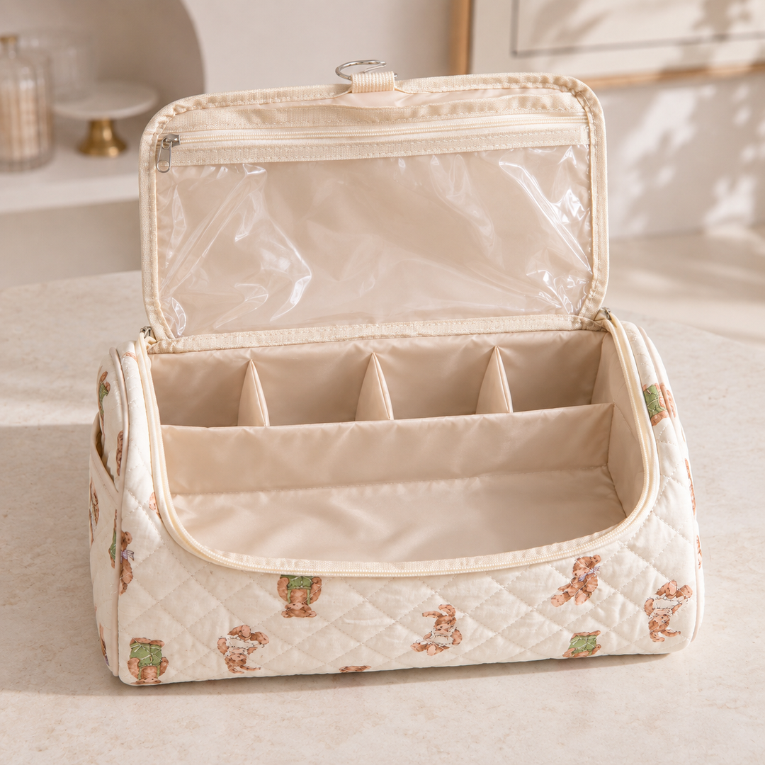 A quilted hair-tool case open on a dressing table, its divided compartments and clear lid pocket empty and visible