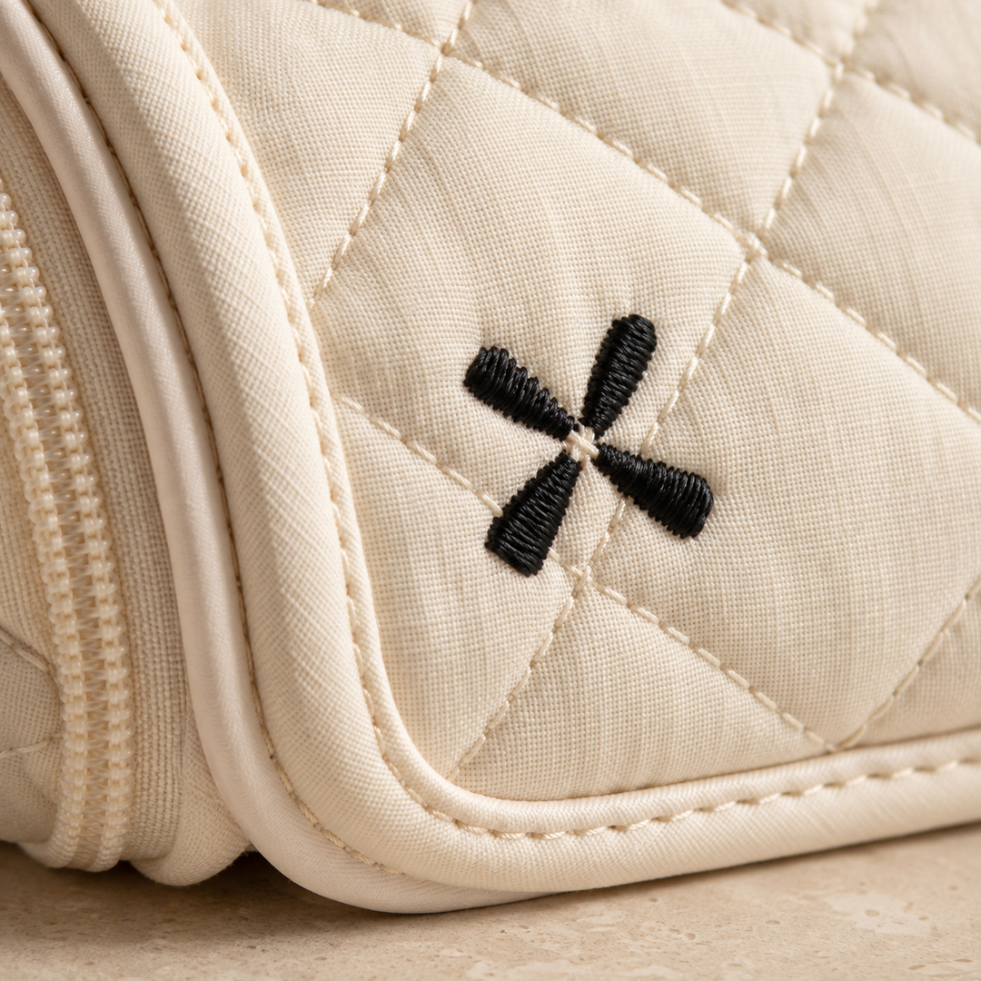 Close-up of diamond quilting, a bound edge and an embroidered four-stroke motif on a cream hair-tool case