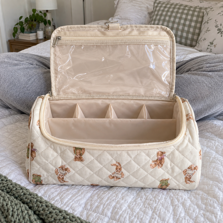 A teddy-print hair-tool case open flat on a bed beside a woman sitting cross-legged