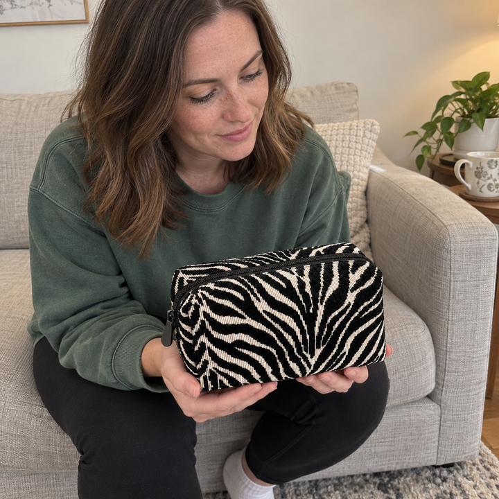 AI illustration: a woman in a green sweatshirt sits in an armchair holding a black and cream zebra pouch.